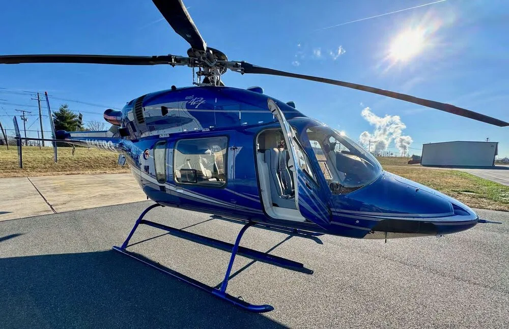 A blue Bell 427 helicopter with its doors open is parked on an airfield on a sunny day.