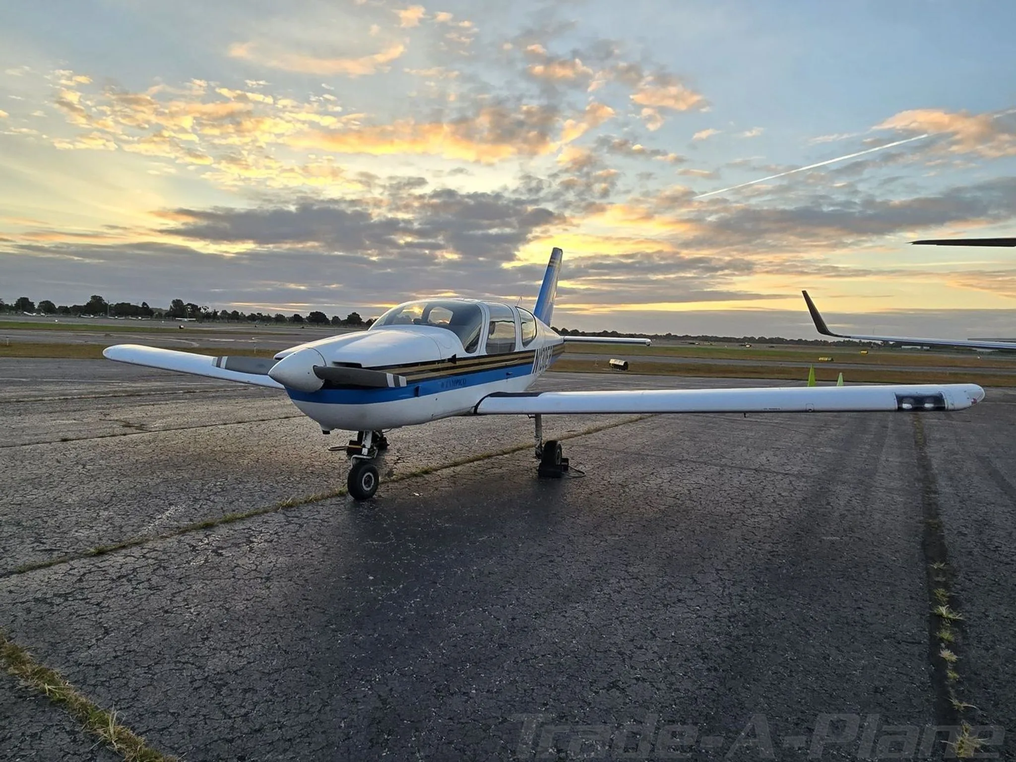 The white and blue Socata TB-9 Tampico N130ER aircraft parked on an airfield at sunset.