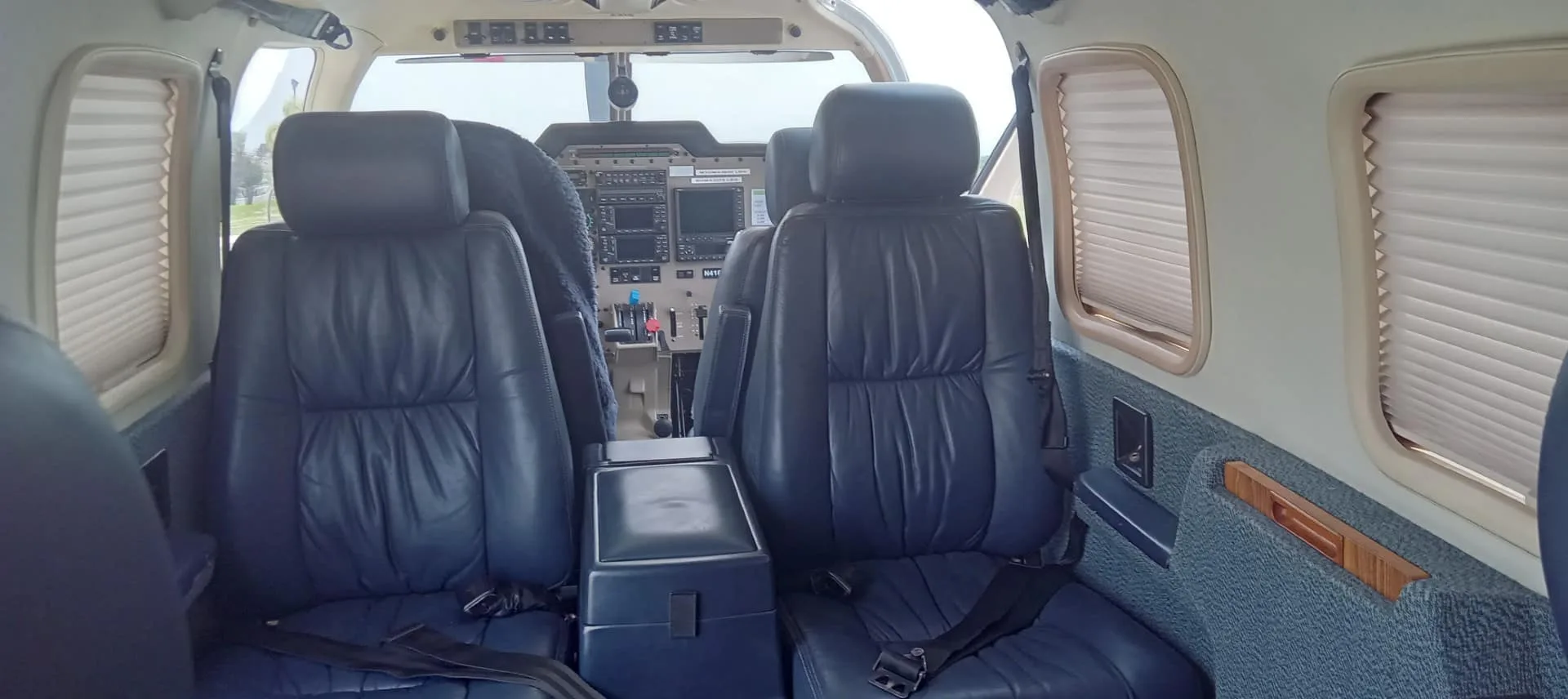 View from the rear cabin of a small aircraft, showing dark blue leather seats and the cockpit beyond.
