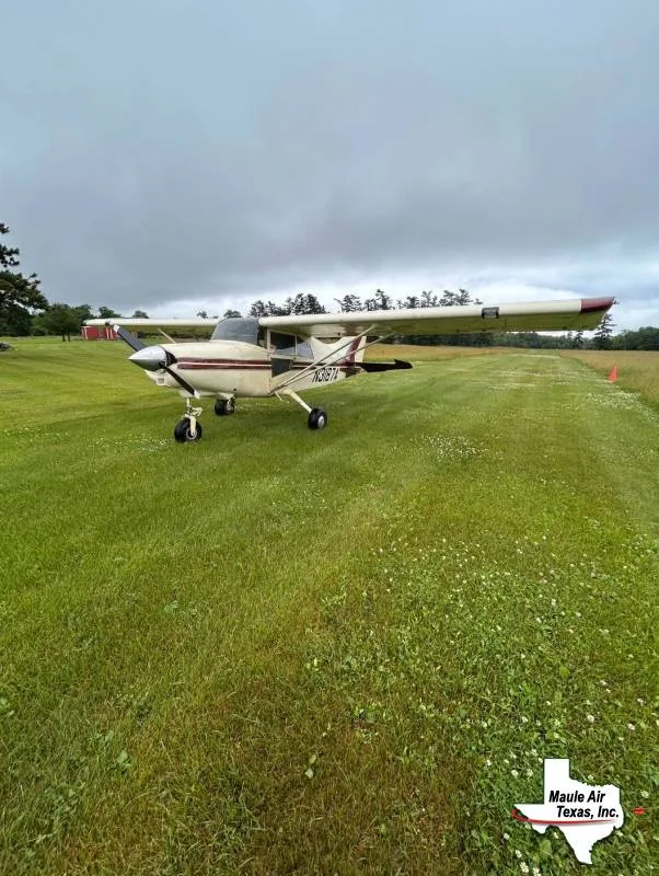 A cream and red light single-engine aircraft, N3871, parked on a grassy airstrip under an overcast sky.