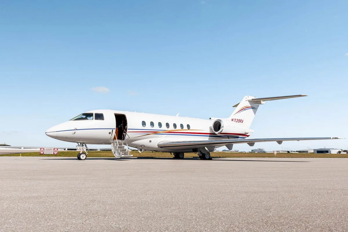 A white Hawker 800XP business jet with red and blue stripes, registration N339RA, parked on the tarmac with its door open and stairs extended.