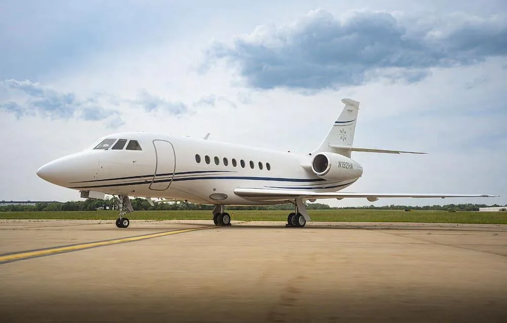A Dassault Falcon 2000 business jet, registration N192HA, parked on an airfield under a cloudy sky.