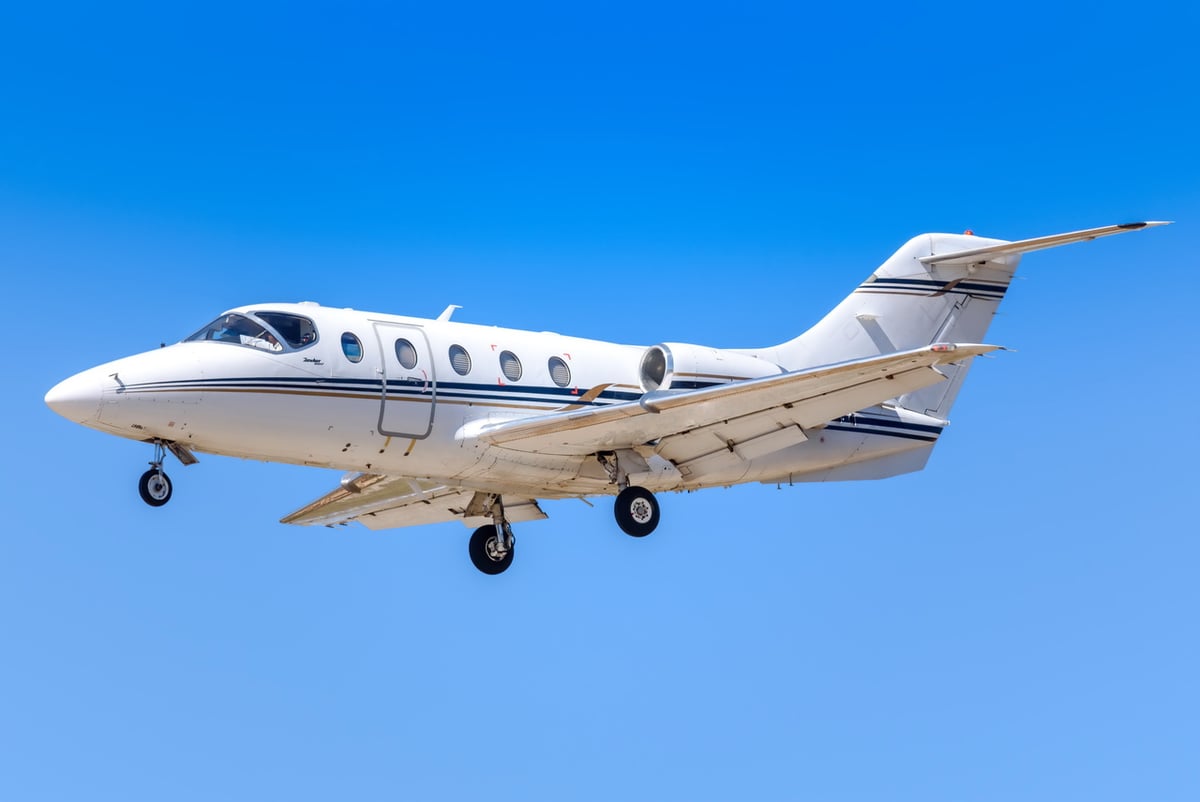 A white jet aircraft in flight with landing gear down against a blue sky.