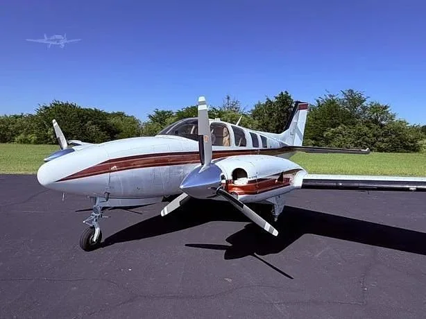 A white and maroon twin-engine propeller aircraft is parked on an asphalt tarmac under a clear blue sky.
