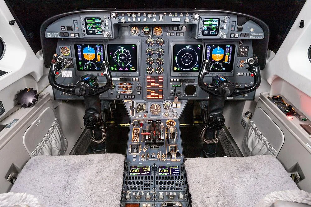 The cockpit of a business jet with multiple digital displays, analog gauges, and control yokes.