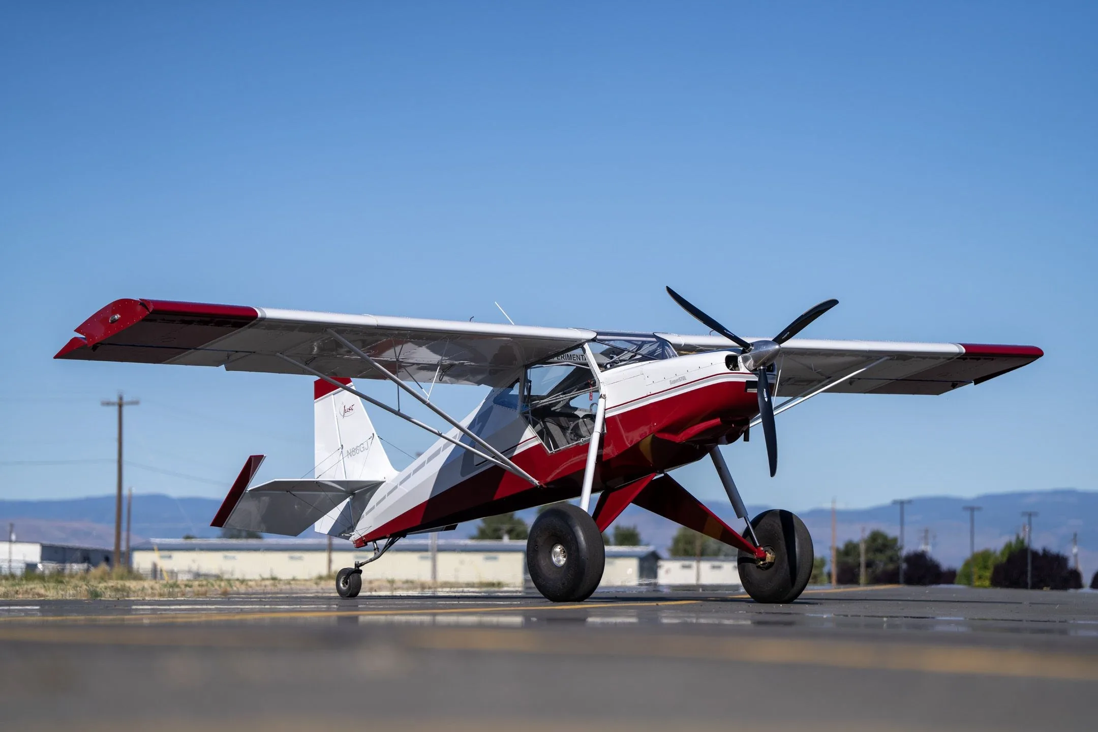 Front-right low angle view of a red and white Just Aircraft SuperSTOL with large tundra tires on an airfield.