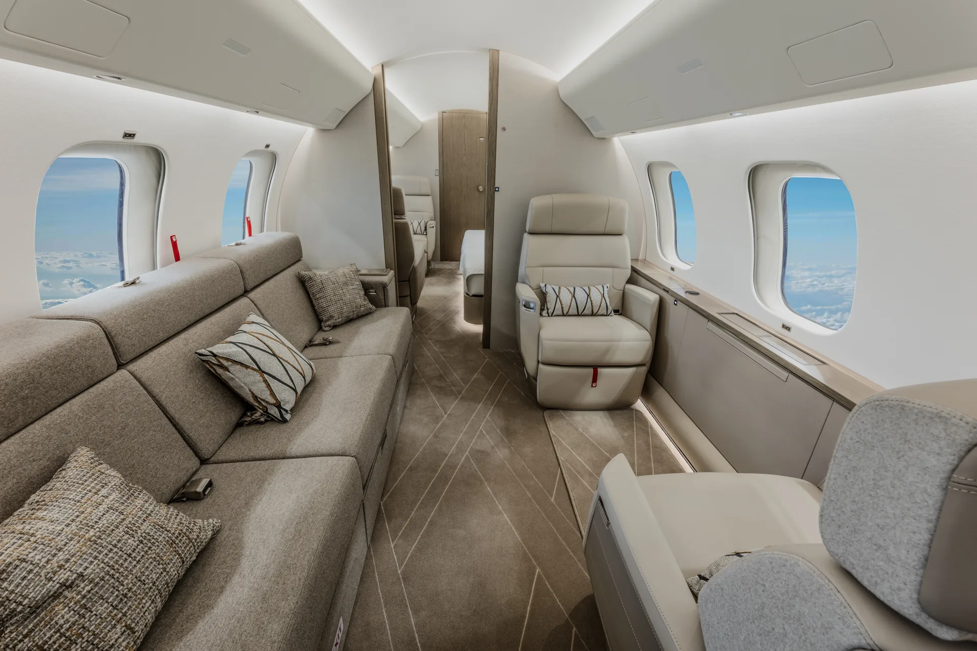 A private jet cabin with a long grey sofa on the left and a single cream leather seat on the right.