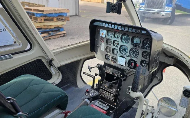 The cockpit of a helicopter features a detailed instrument panel, controls, and green seats.