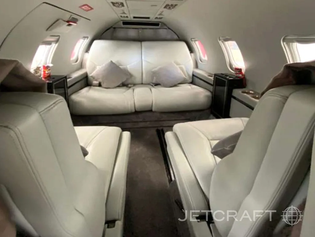 The interior cabin of a private jet with light grey leather seats and a comfortable two-seat sofa at the back.
