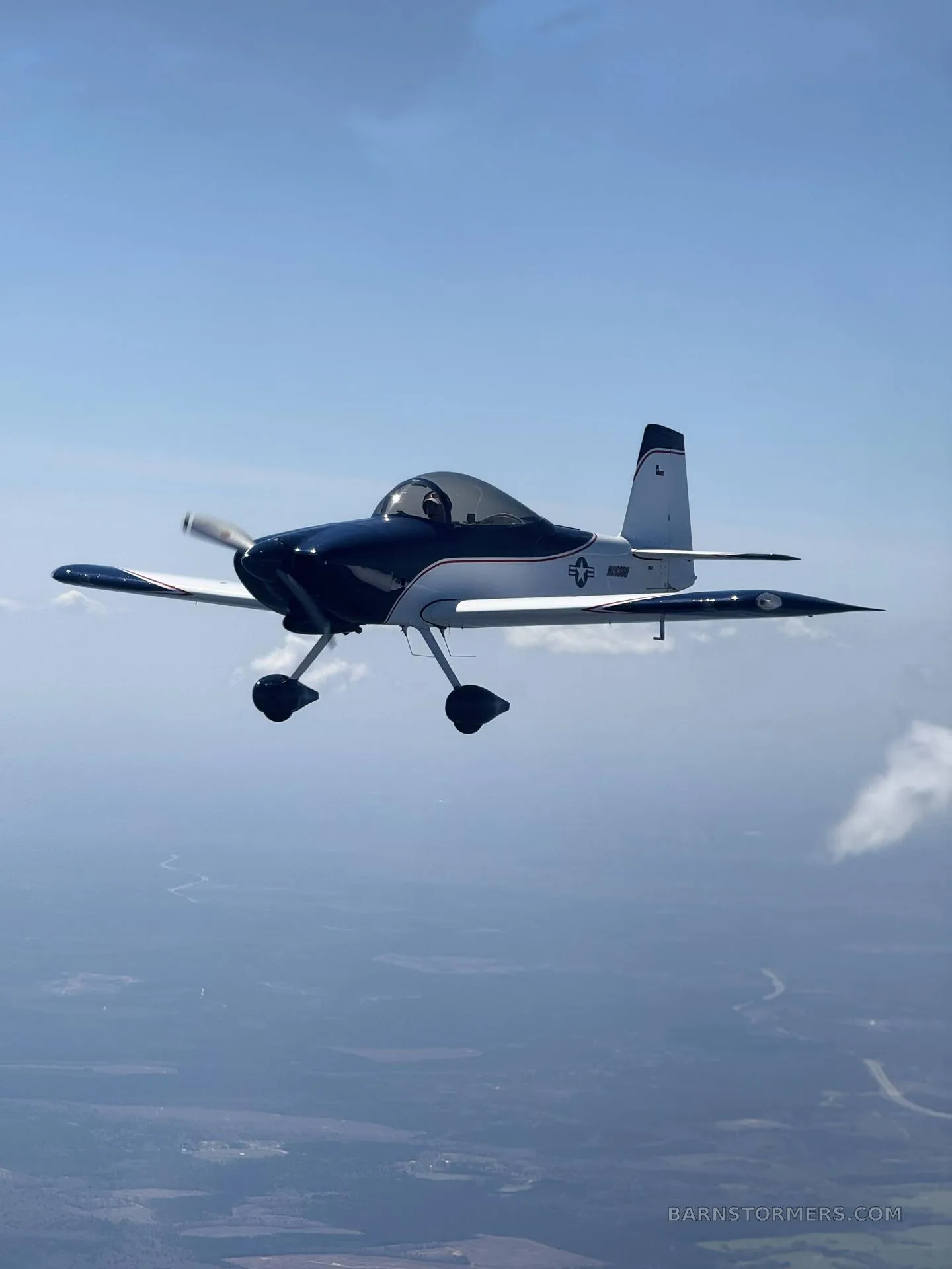 A blue and white single-engine aircraft with a bubble canopy, registration N663BH, flying over a landscape.