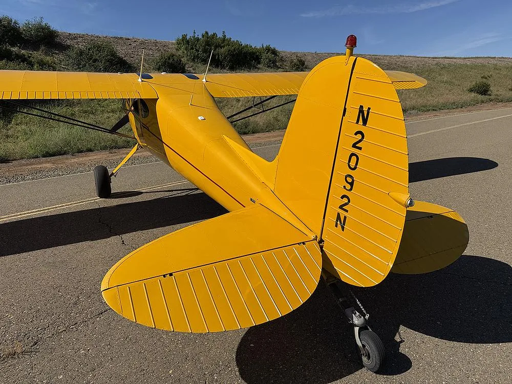Rear-quarter view of the yellow high-wing aircraft N2092N, showing the tail, horizontal stabilizer, and landing gear.