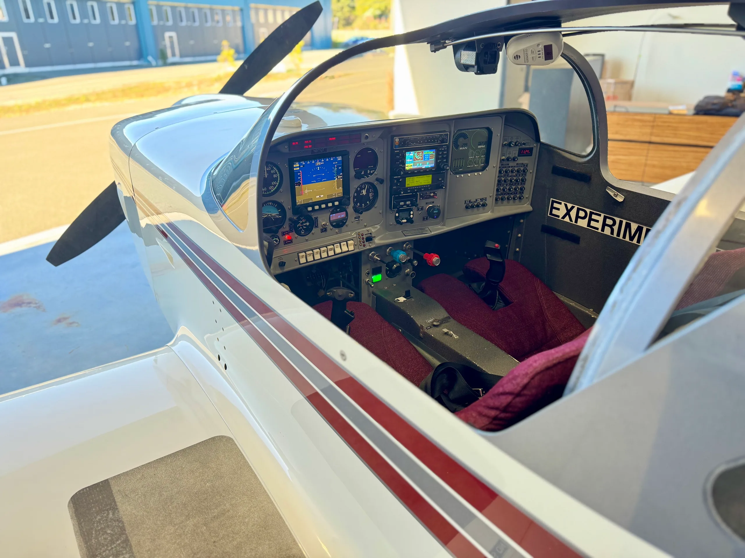 A view into the cockpit of a white aircraft, showing the instrument panel with multiple screens and controls, and red seats.