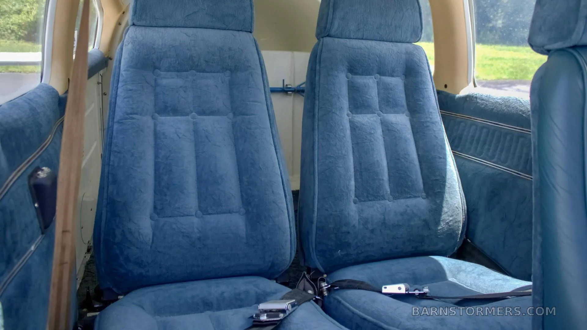 Two blue upholstered passenger seats with seatbelts in the interior cabin of a light aircraft.
