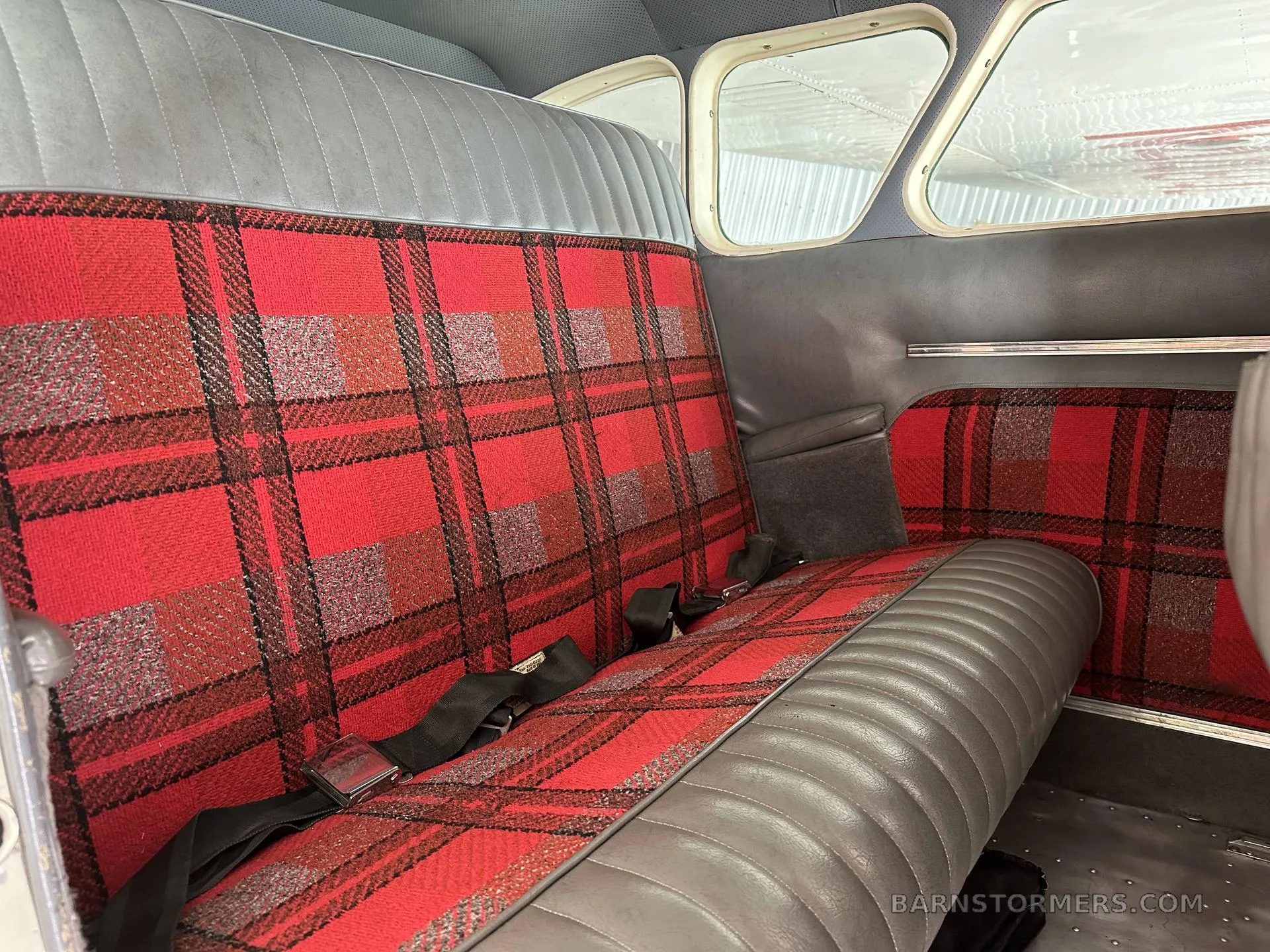 The rear cabin interior of an aircraft, featuring gray and red plaid upholstered seats with seatbelts.