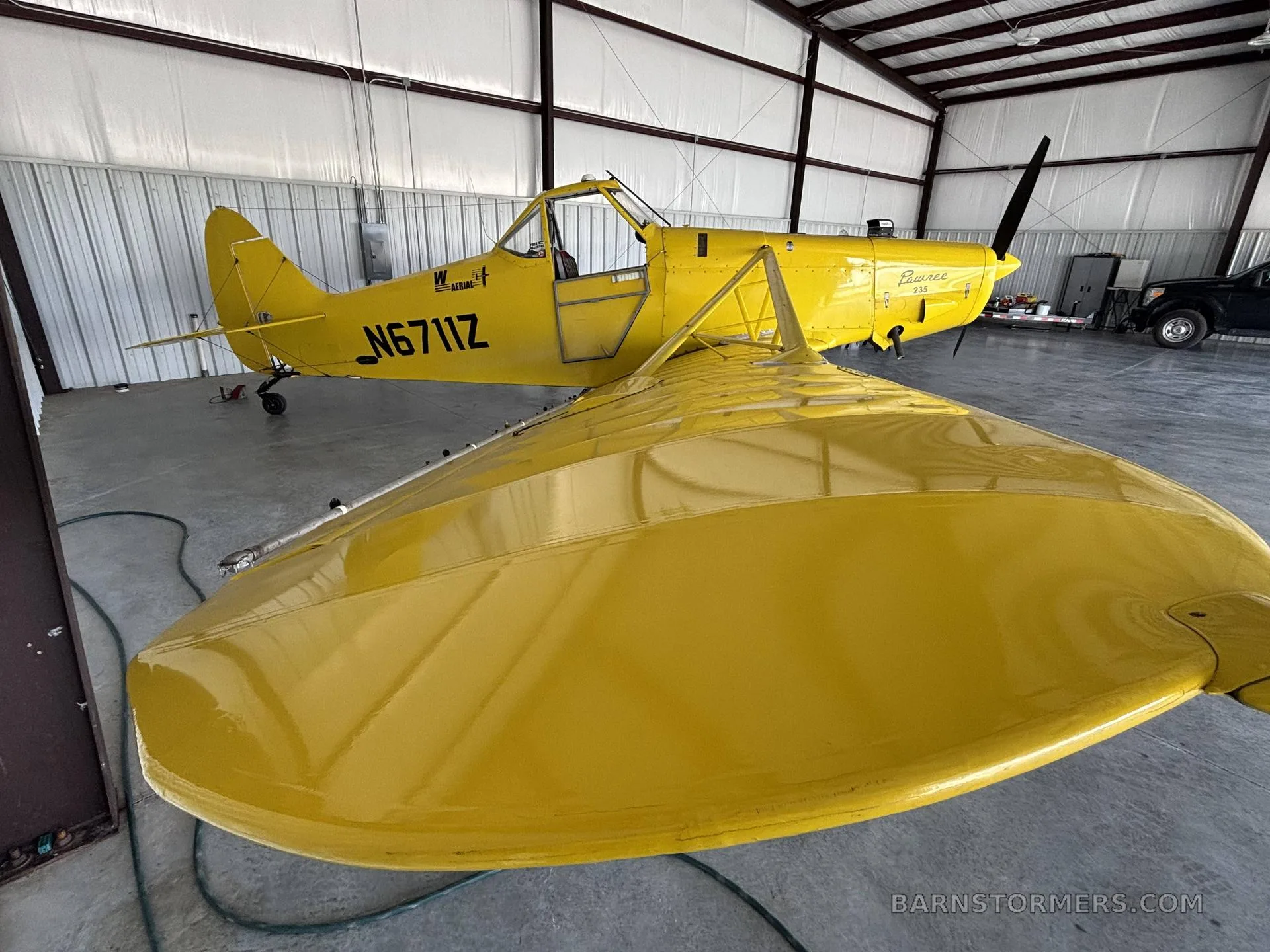 A yellow Piper PA-25 Pawnee aircraft with registration N6711Z, viewed from the front-right in a hangar.