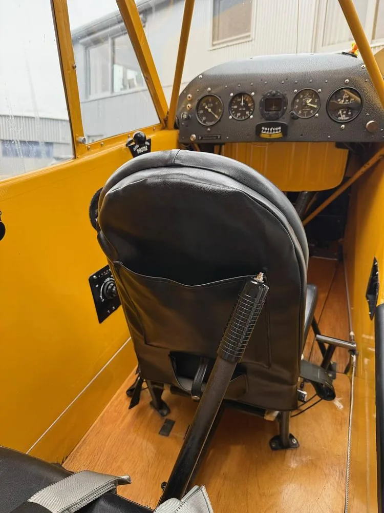 View of the black leather rear seat and wooden floor inside a yellow aircraft cabin, with a partial view of the instrument panel.