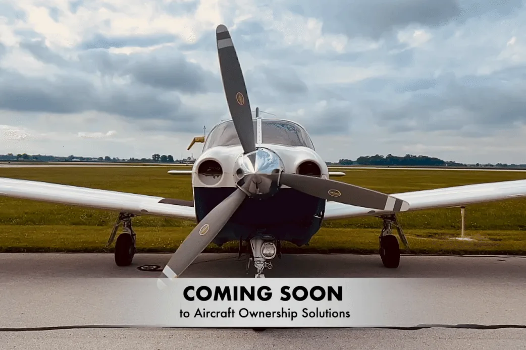Front view of a white and blue twin-engine propeller aircraft parked on an airfield under a cloudy sky.