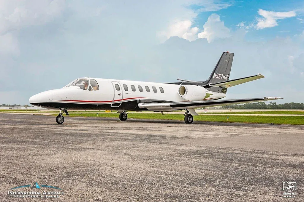 A front-side view of a white and black Cessna Citation business jet (N557MM) parked on an airfield.