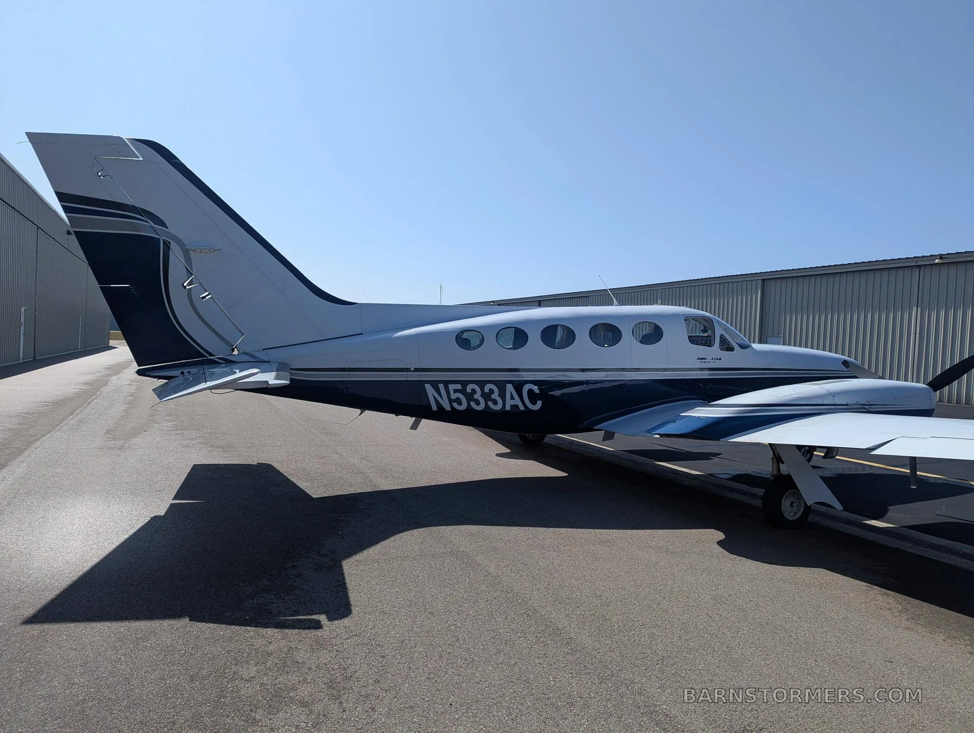 A white and dark blue twin-engine propeller aircraft (Cessna 414 Chancellor) with tail number N533AC parked on an asphalt ramp, viewed from the right side.