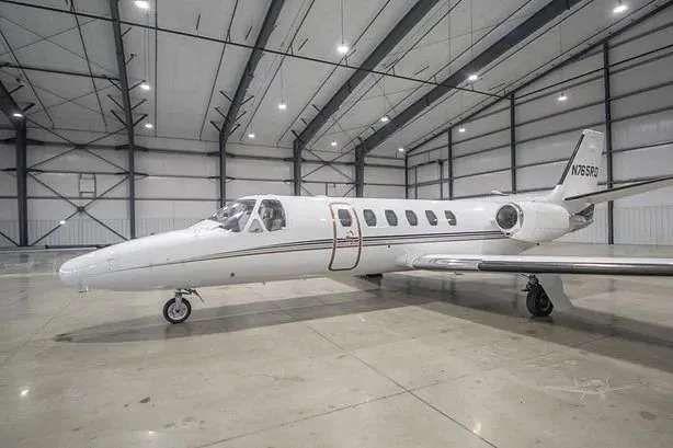 A white business jet with black and gold stripes, tail number N765RD, is parked inside a large hangar.