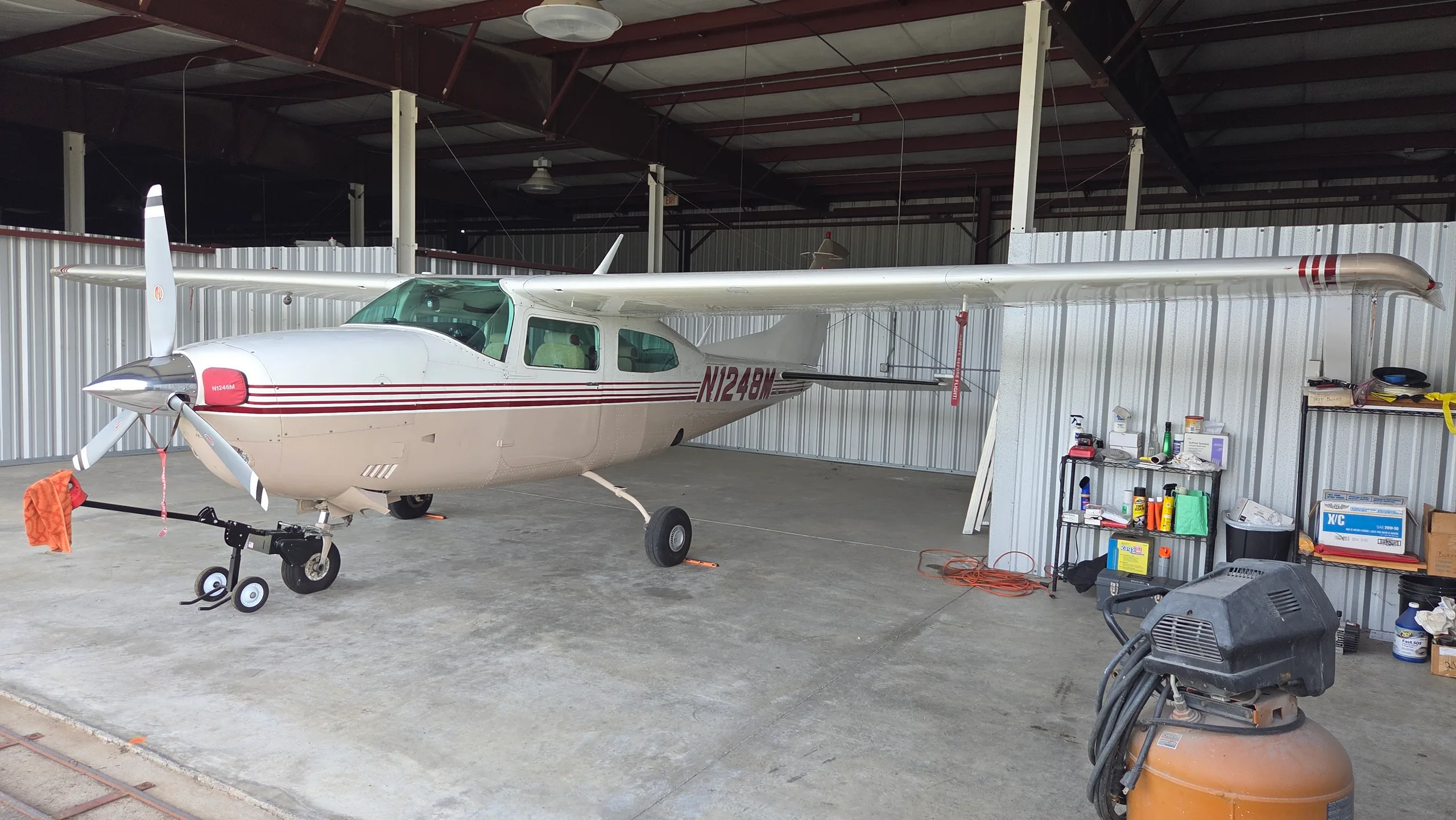 A side view of a white and tan single-engine propeller aircraft with red stripes and registration N1248M, parked in a hangar.