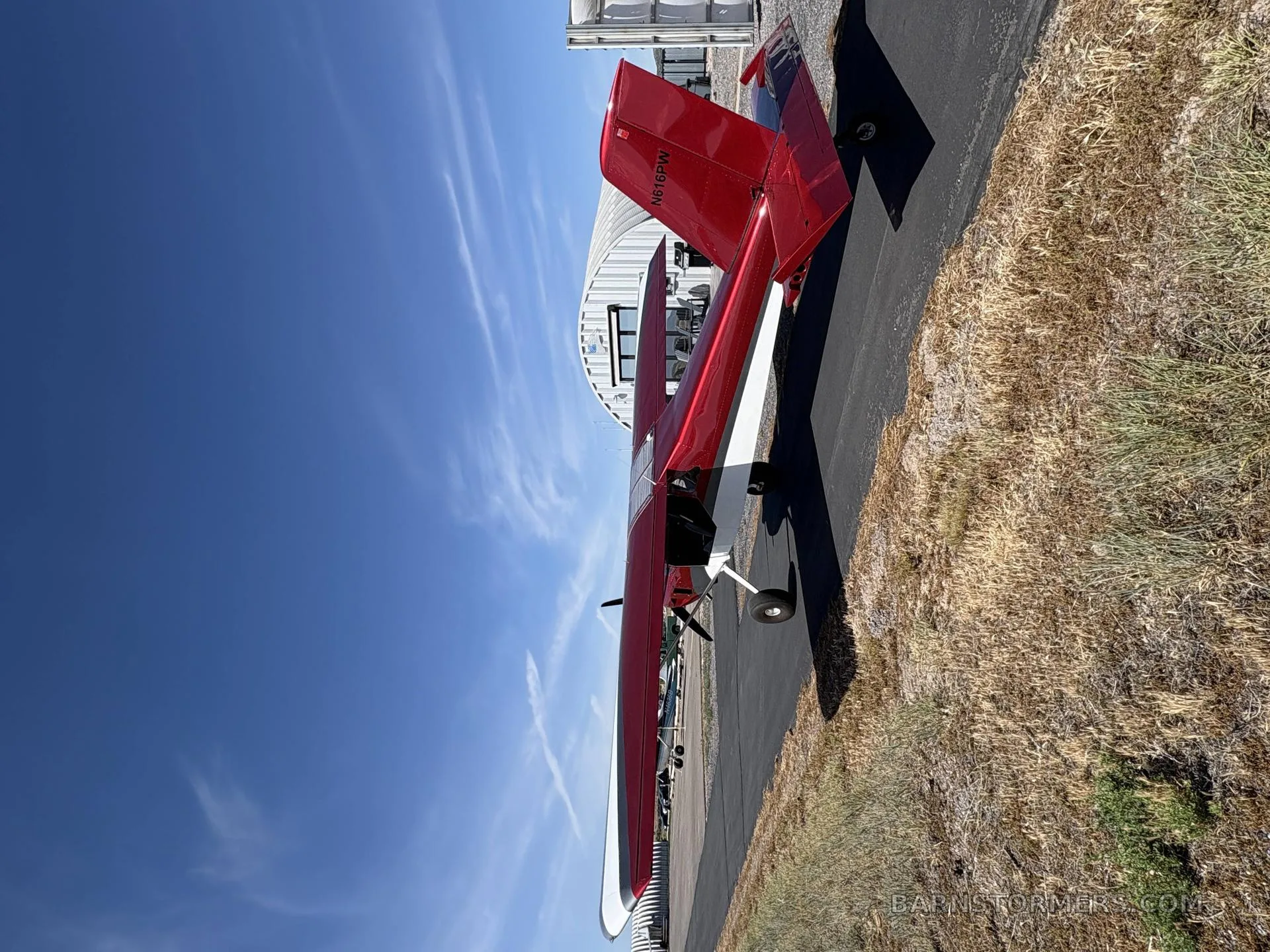 A red and white single-engine aircraft with tail number N616PW on an asphalt strip, viewed from the rear with a hangar in the background.
