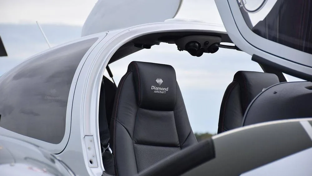 The black leather interior seats of a Diamond aircraft, with the "Diamond Aircraft" logo embroidered on the headrest.