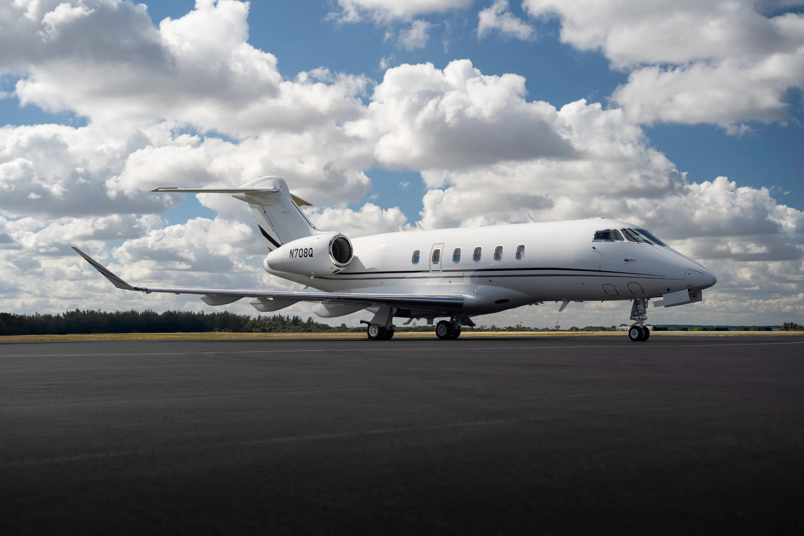 A white business jet with tail number N708Q is parked on a tarmac under a partly cloudy sky.
