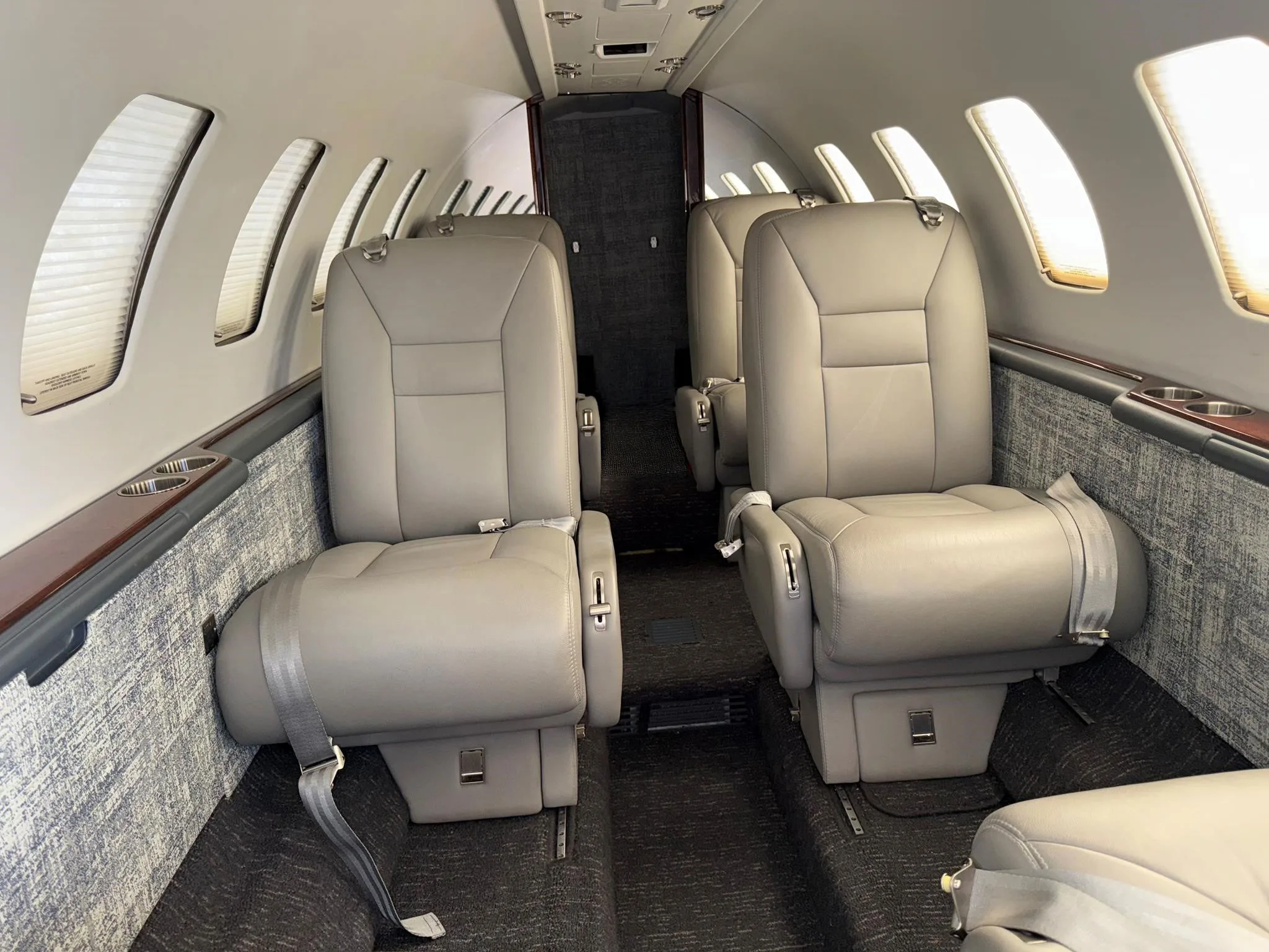 The interior cabin of a private jet with light grey leather seats and dark grey carpet.
