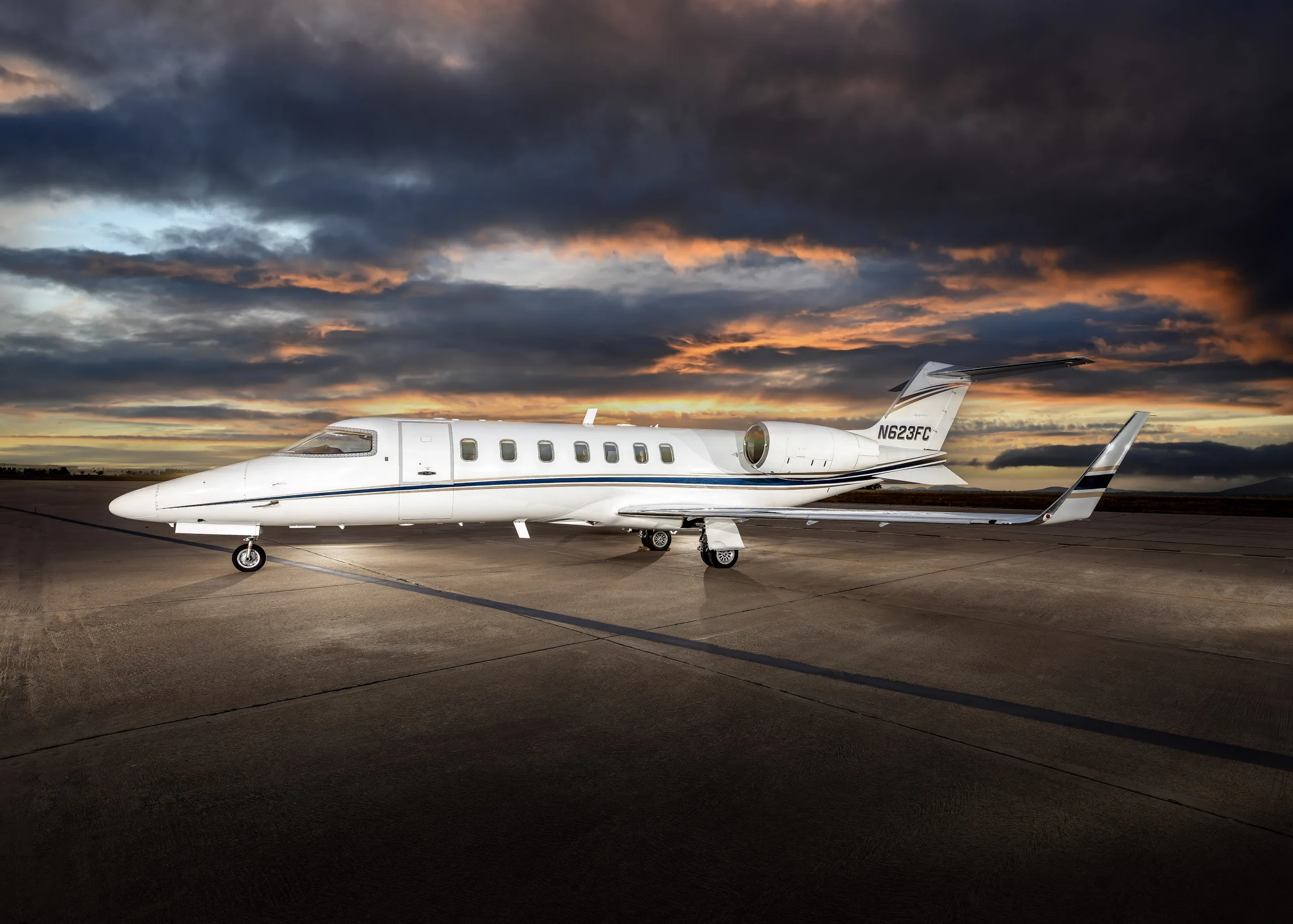 A white Learjet 60 with a blue stripe, registration N623FC, parked on an airfield at sunset.