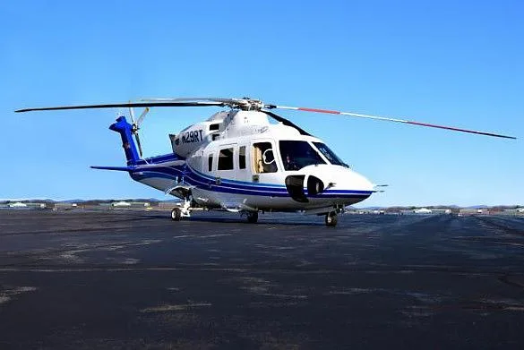 A white and blue Sikorsky S-76 helicopter (N29RT) is parked on a tarmac under a clear blue sky.