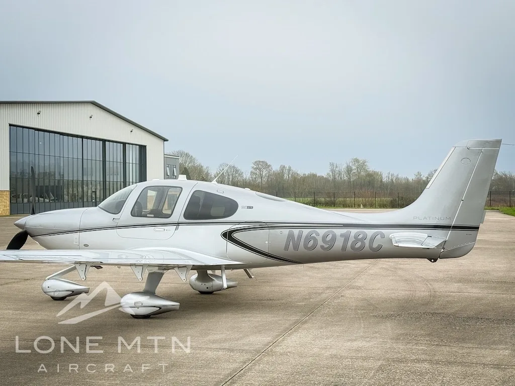 Side view of a silver Cirrus SR22 aircraft, registration N6918C, parked next to a hangar.