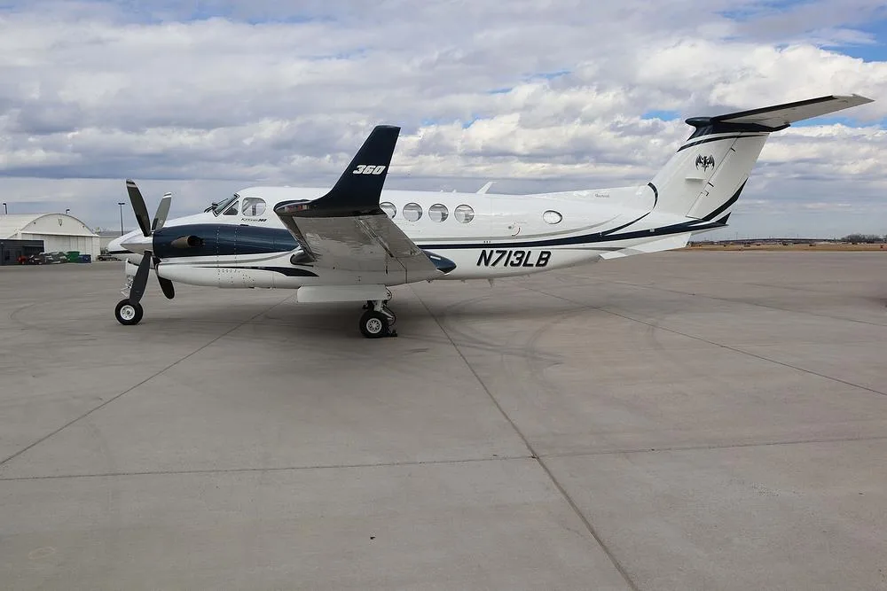 A three-quarter rear view of the white and dark blue Beechcraft King Air 360, registration N713LB, on an airport tarmac.
