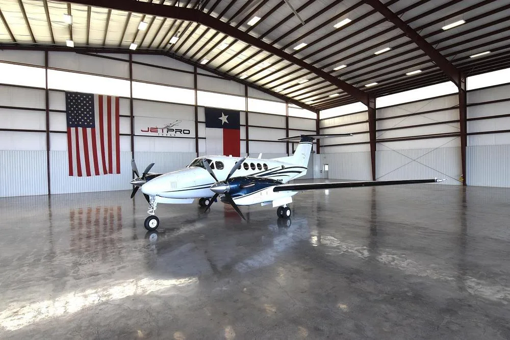 A front-right view of the white and blue Beechcraft King Air twin-engine turboprop aircraft, N627MG, in a hangar.