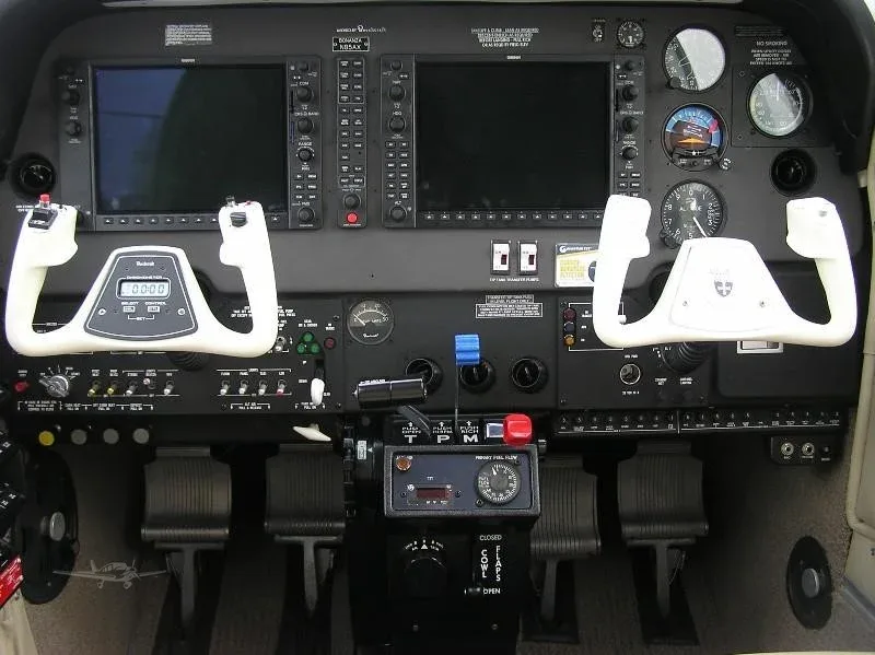 The cockpit of an aircraft featuring two large display screens, dual yokes, and various instruments and controls.