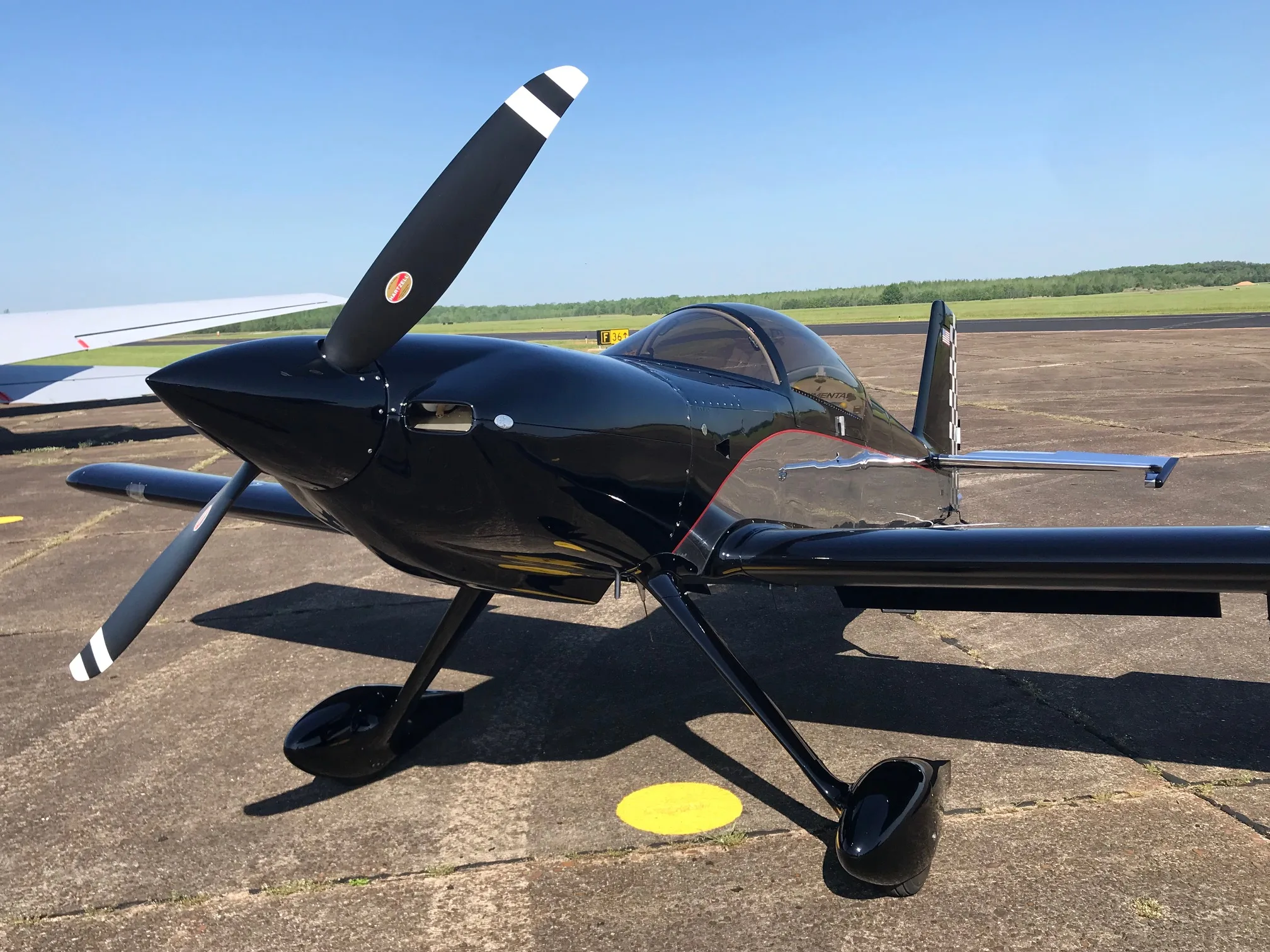 A close-up side view of a black experimental aircraft with a two-bladed propeller on an airfield.