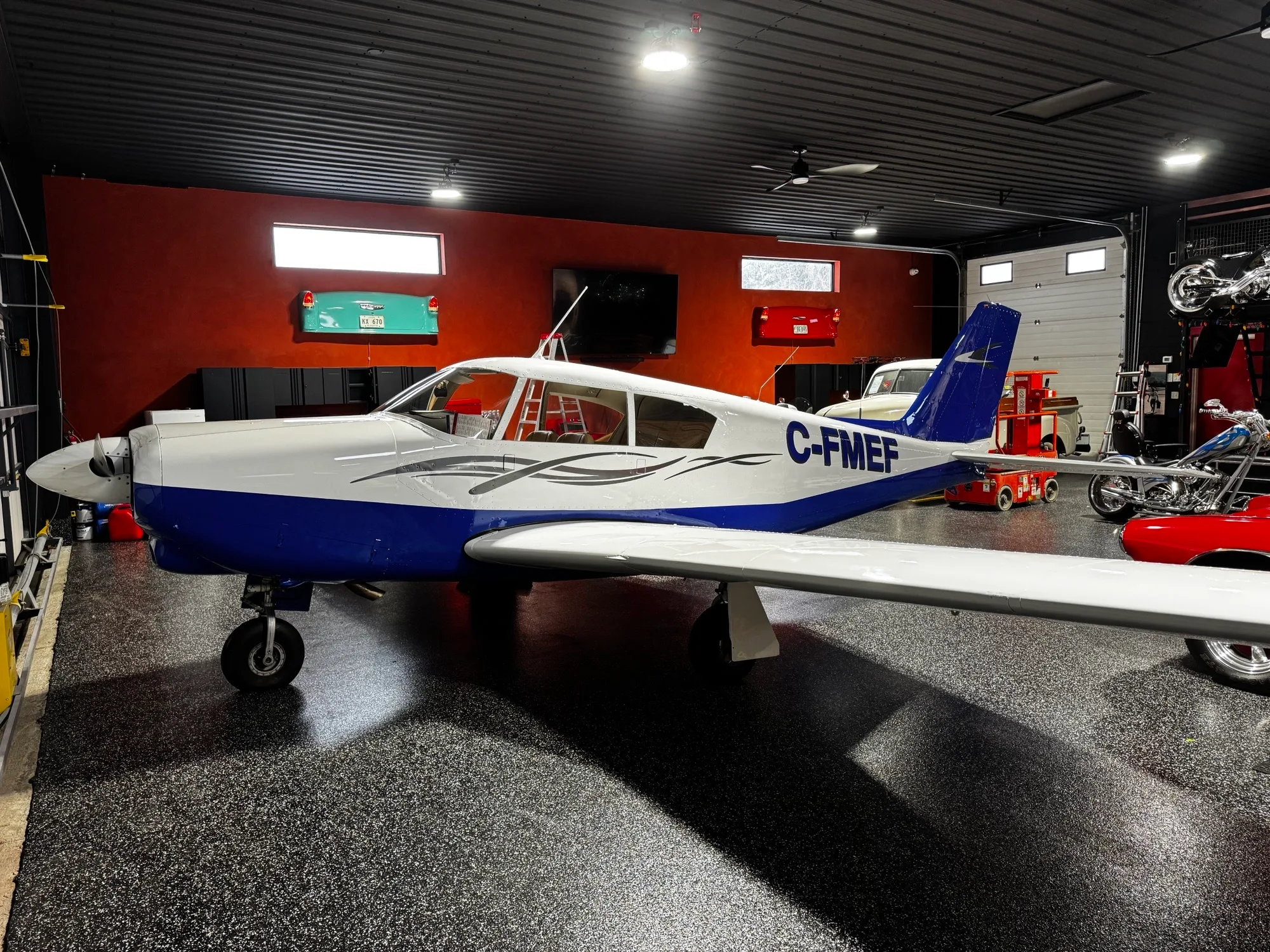 A white and blue single-engine propeller aircraft, registration C-FMEF, parked in a well-lit garage.