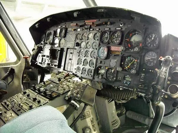 The detailed instrument panel and controls of a helicopter cockpit are shown from the pilot's perspective.