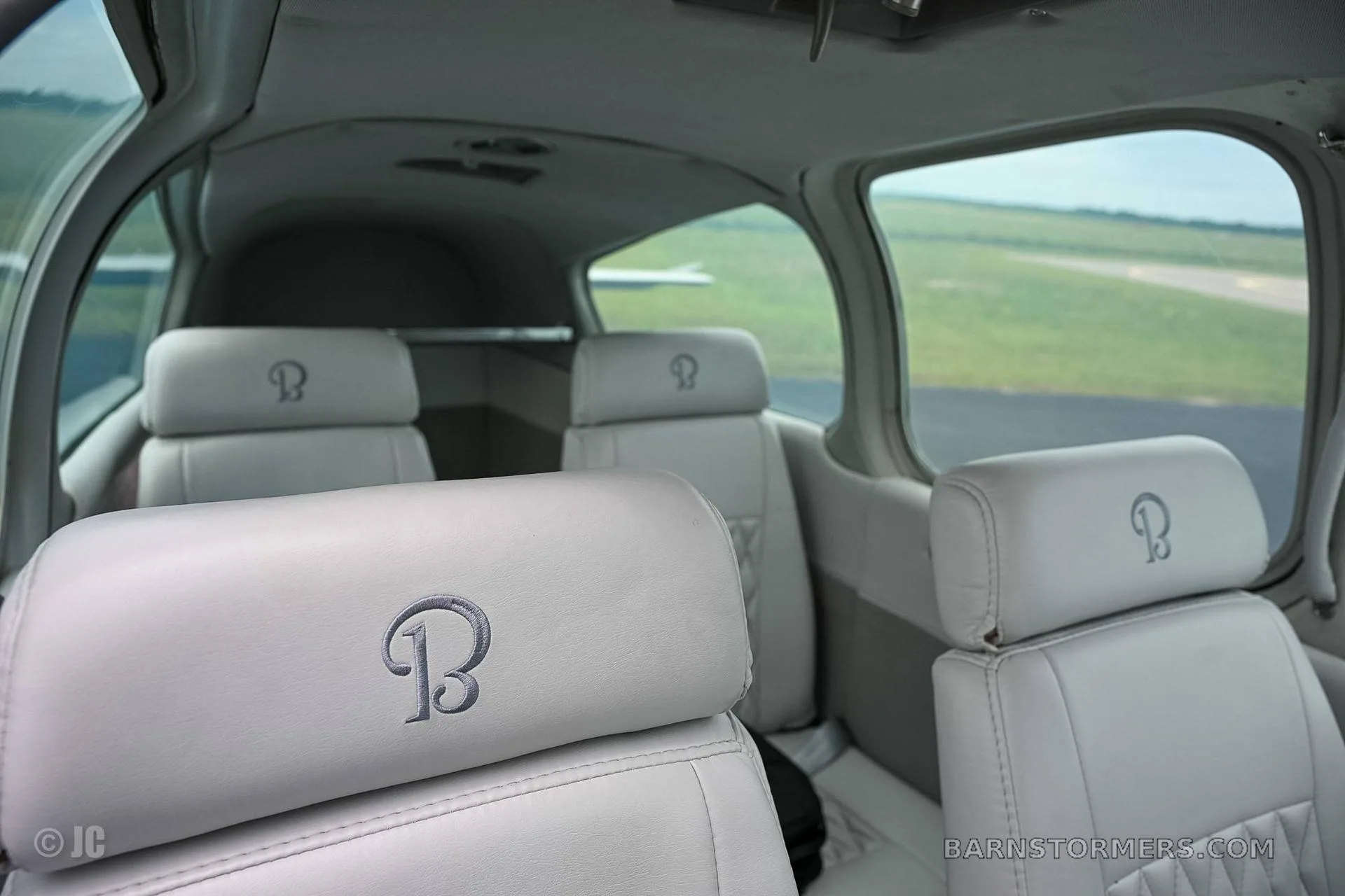 The light gray leather interior of an aircraft cabin with seats featuring an embroidered 'B' logo, looking towards the rear.