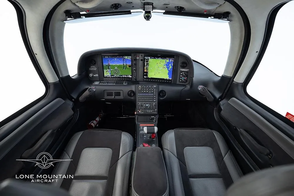 The cockpit of a modern aircraft, showing two grey seats and multiple digital display screens.