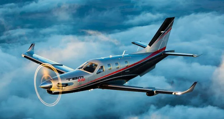 A TBM 930 aircraft in flight against a cloudy sky.