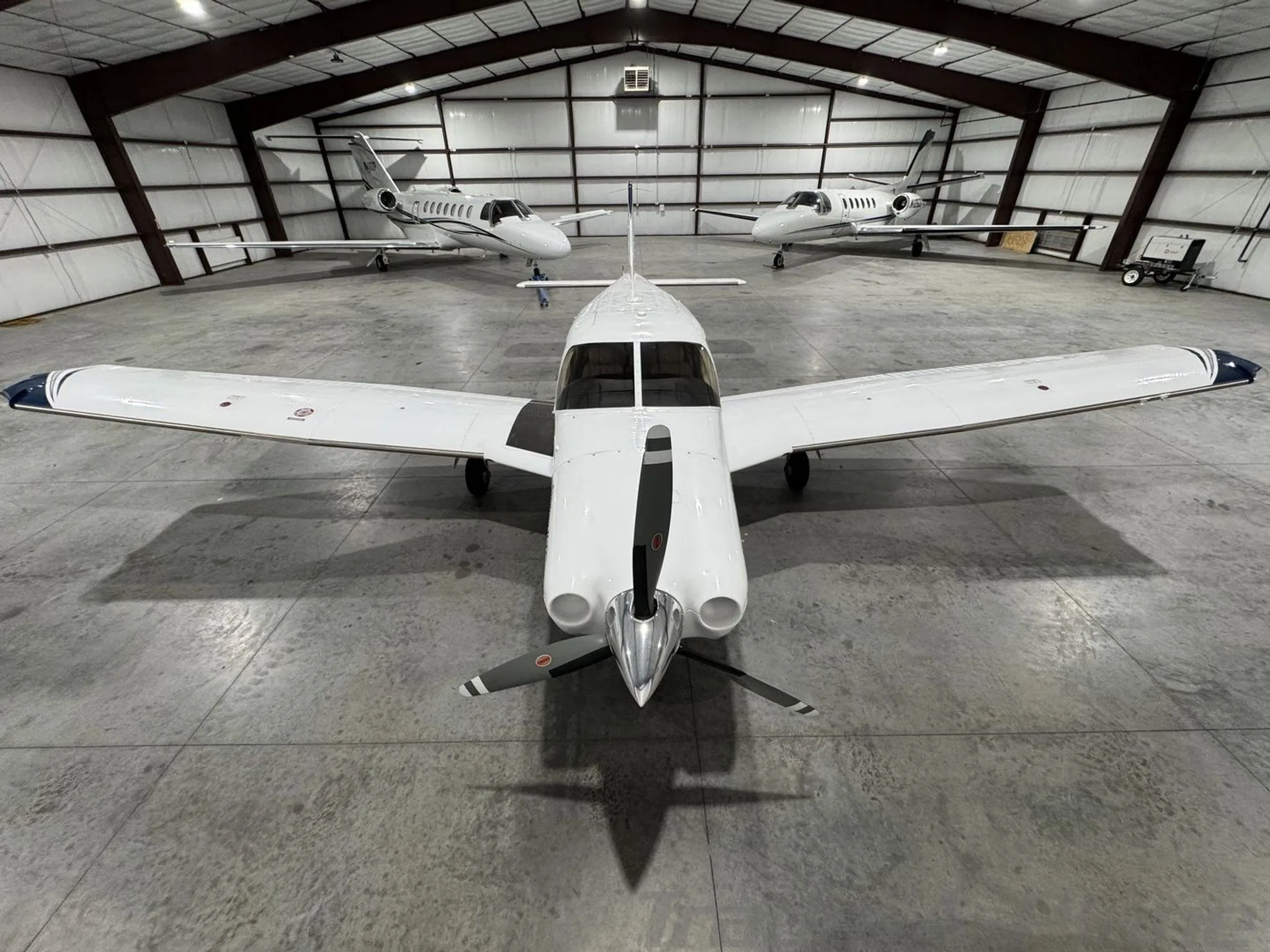 A head-on view of the Piper Saratoga II TC N436MA with its propeller, parked in a hangar between two jets.