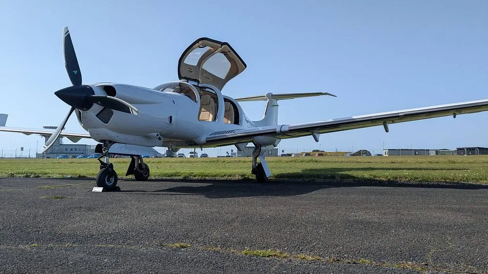 A white propeller aircraft with its canopy doors open, parked on an airfield.
