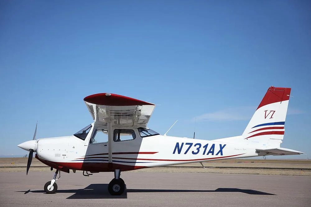 A white and red single-engine propeller aircraft, N731AX, with its engine cowling open, parked on an airfield.