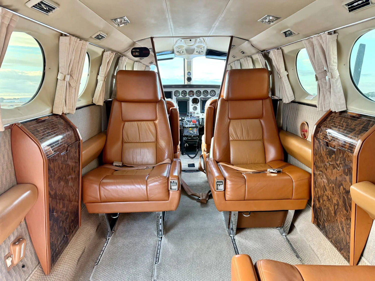 The aircraft's cabin interior features two rows of brown leather seats and wood trim, with the cockpit visible forward.