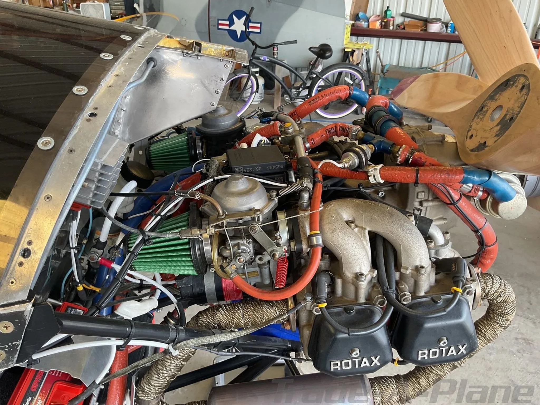 A detailed view of the Rotax aircraft engine with various hoses, wires, and air filters, exposed in a hangar.