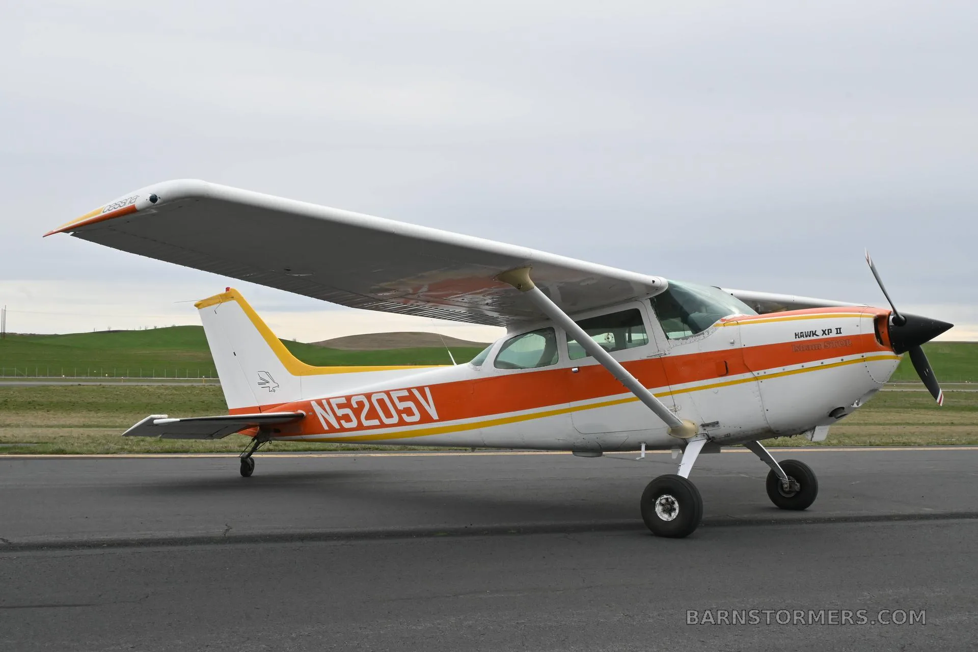 A white and orange Cessna 172 Hawk XP II (N5205V) parked on an asphalt runway, viewed from the right side.