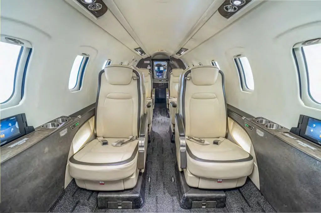 The interior cabin of a business jet, featuring two rows of light beige leather seats facing forward.