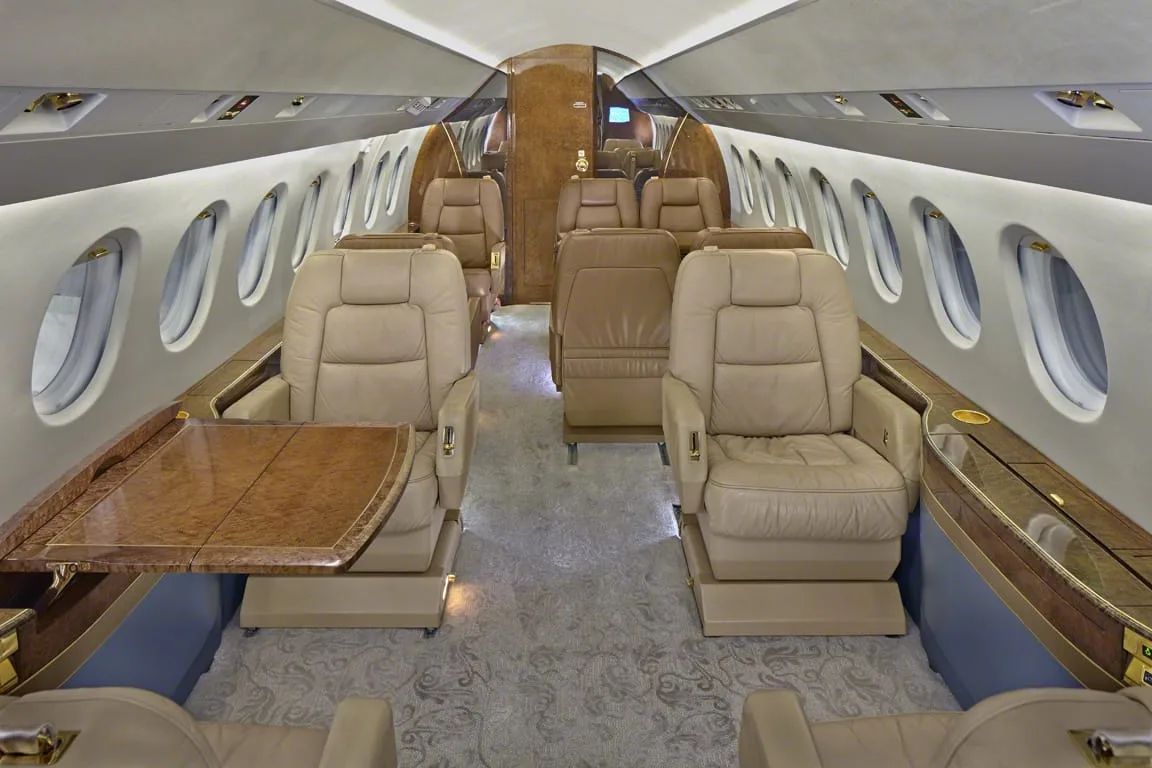 The luxurious cabin interior of a private jet with beige leather seats and a wooden table.