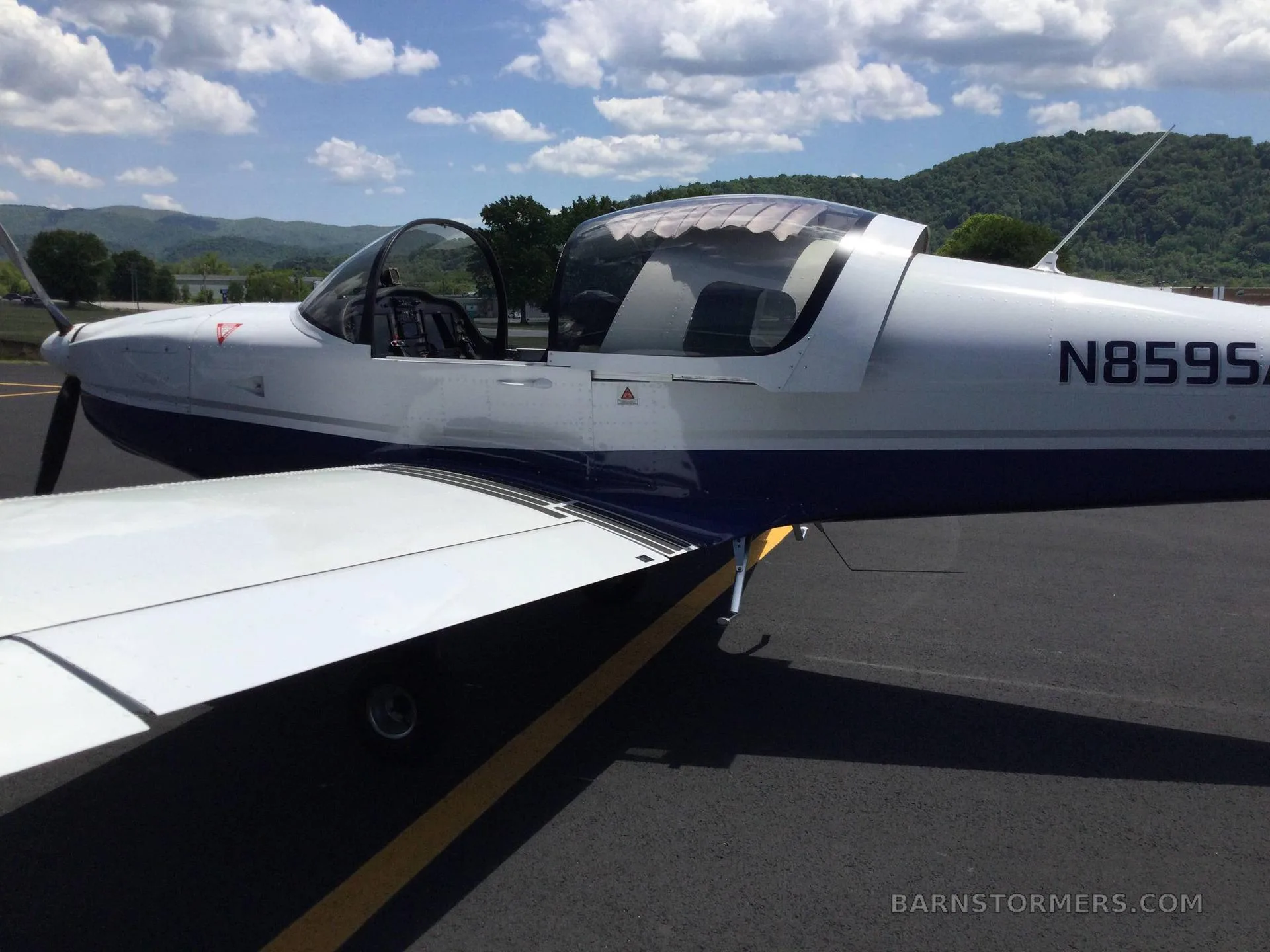A white and blue Sling aircraft with registration N859SA is parked on an asphalt runway, viewed from the side with the canopy open.